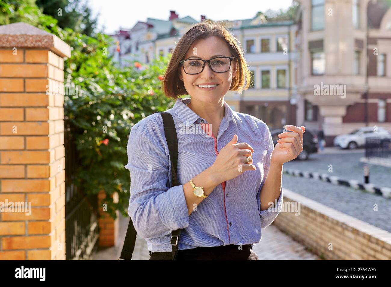 Positivo sorridente donna di affari matura che indossa occhiali blu camicia cercando alla telecamera Foto Stock