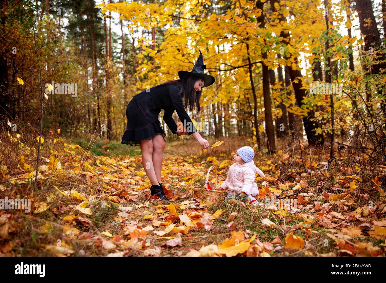 donna strega gioca con un bambino piccolo nella foresta d'autunno. halloween concetto costumi. strega e coniglietto. concetto di amici madre e figlia Foto Stock
