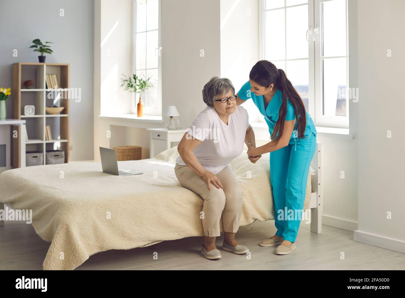 La donna che si prende cura di una donna anziana in una casa di cura la aiuta a uscire dal letto. Foto Stock