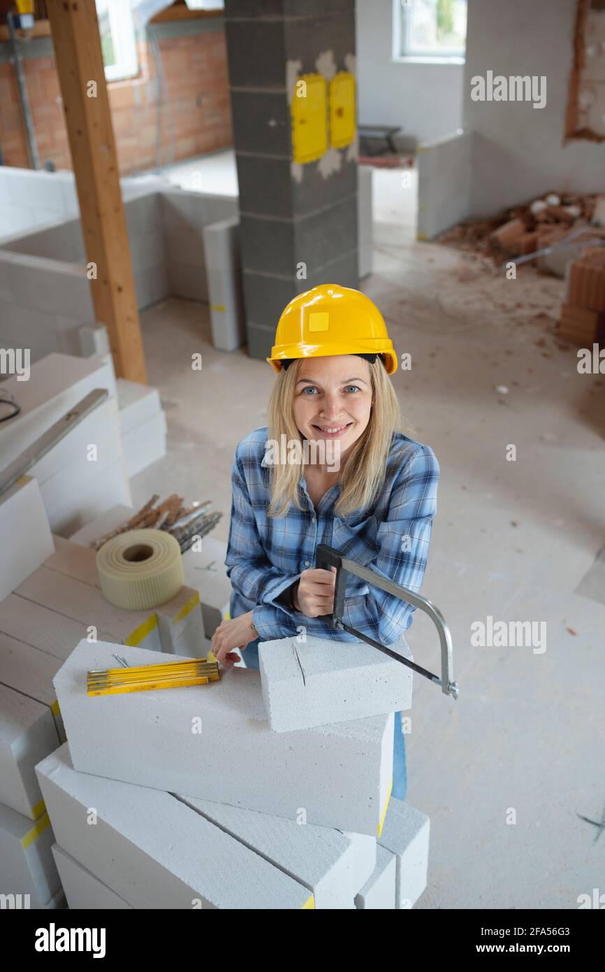 bella giovane muratore femminile con elmetto di sicurezza giallo sta  segando mattoni su un luogo di costruzione nella casa ed è felice Foto  stock - Alamy