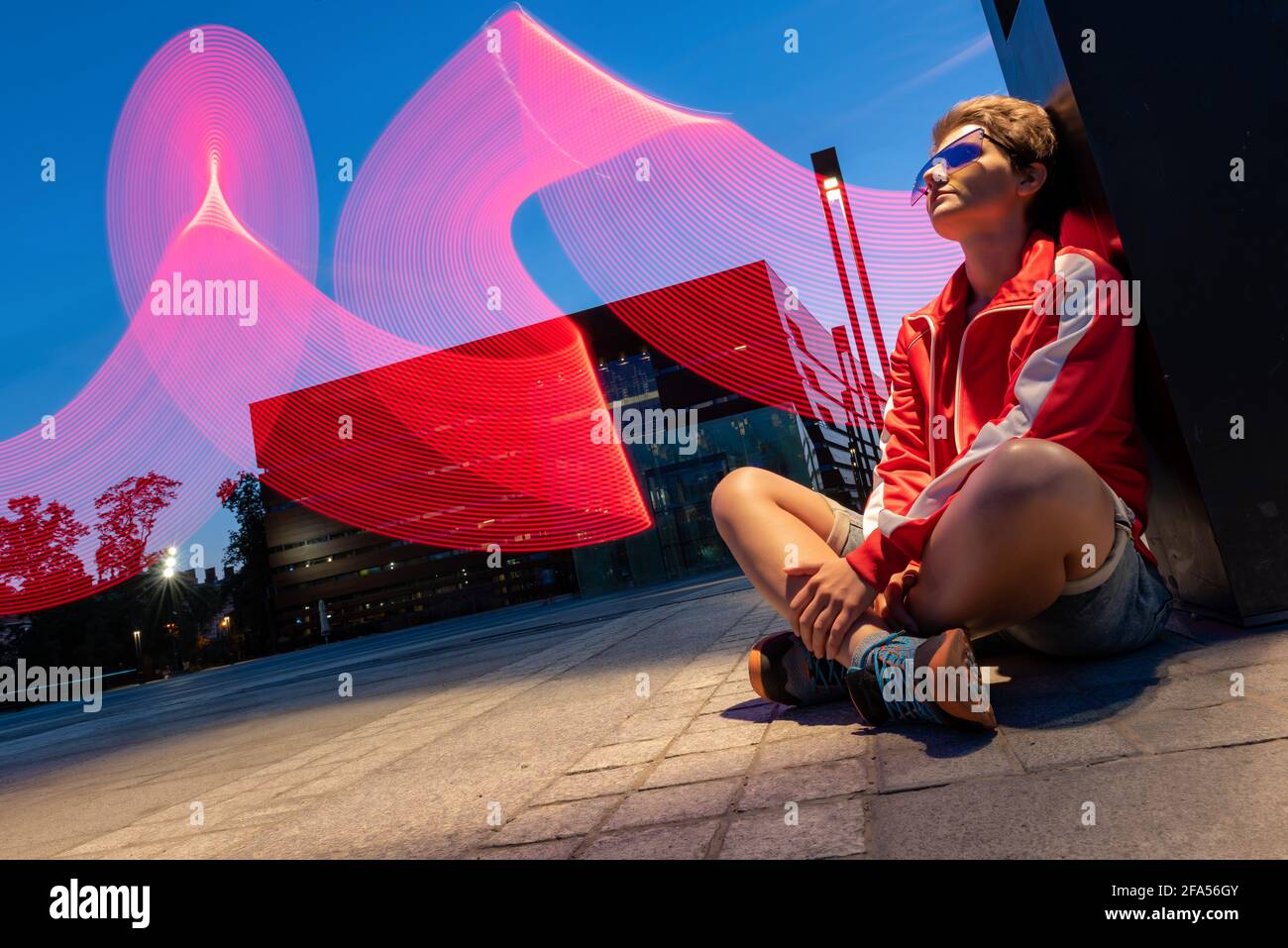 ritratto di giovane donna seduta all'aperto su un terreno a lunga esposizione. giovane donna che indossa per la festa di tecno di night club che posa su sfondo con ascessa Foto Stock