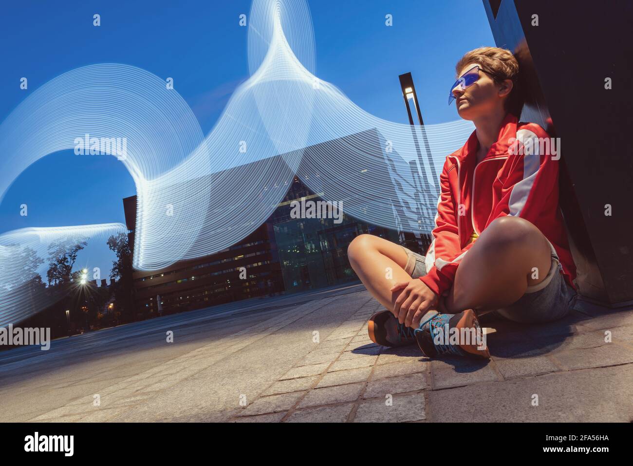 ritratto di giovane donna seduta all'aperto su un terreno a lunga esposizione. giovane donna che indossa per la festa di tecno di night club che posa su sfondo con ascessa Foto Stock