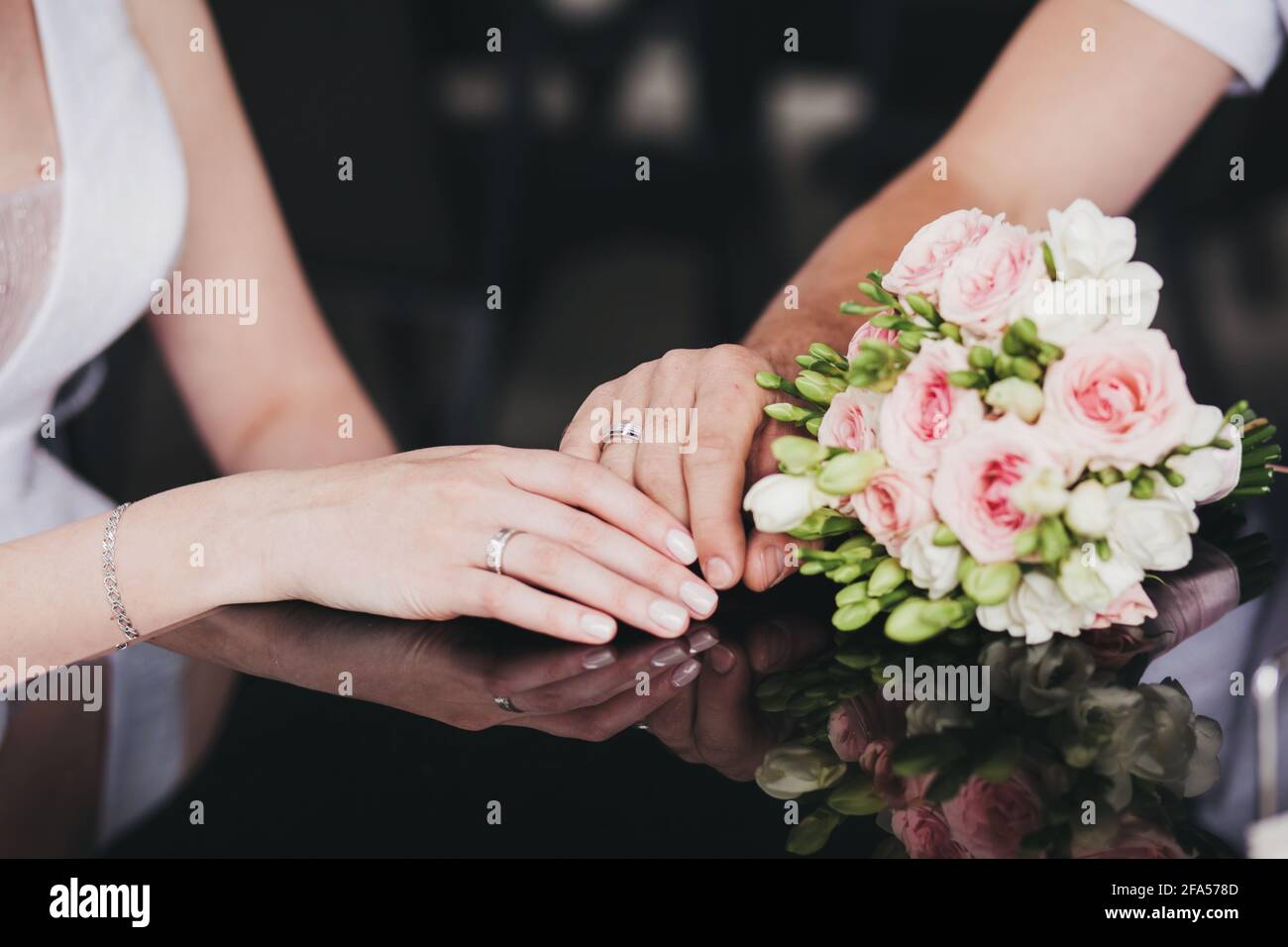 le mani degli sposi novelli sul tavolo del caffè successivo al bouquet della sposa Foto Stock