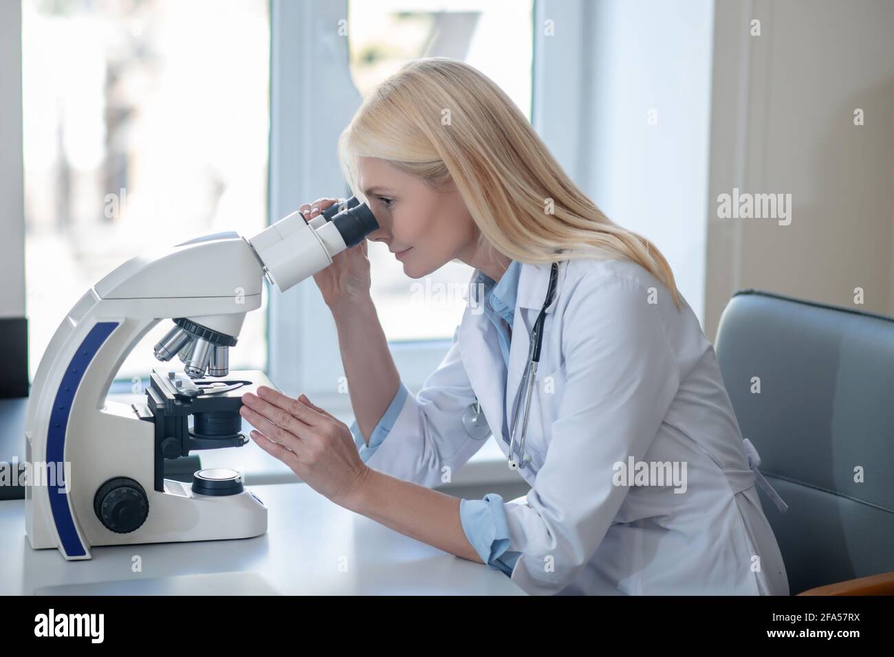 Profilo della donna in uniforme guardando al microscopio Foto Stock