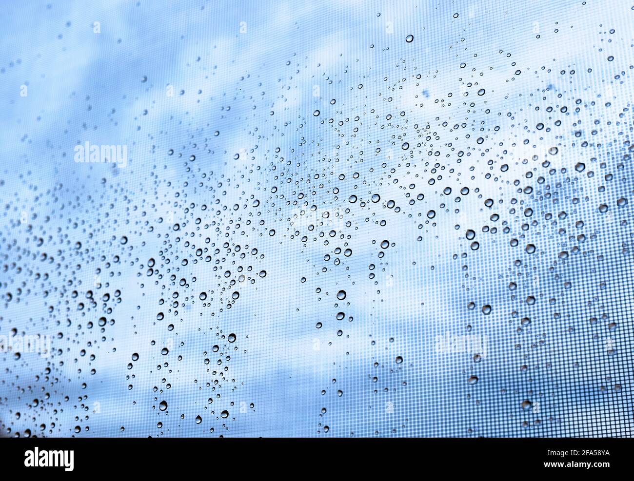 dettaglio di alcune gocce d'acqua su una finestra con un cielo blu e nuvoloso Foto Stock
