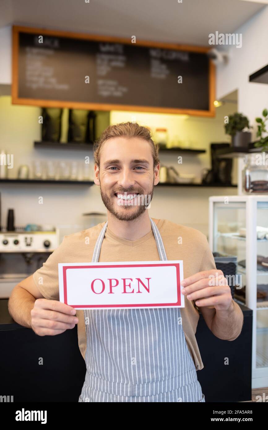 Felice ottimista uomo che tiene il cartello Open in cafe Foto Stock