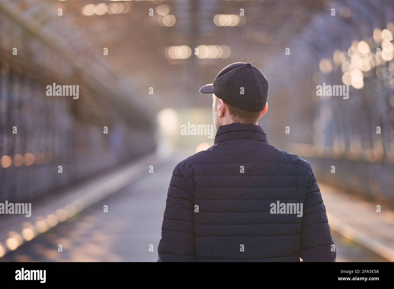 Persona sola che cammina sul ponte all'alba. Vista posteriore di un giovane adulto con cappuccio. Foto Stock