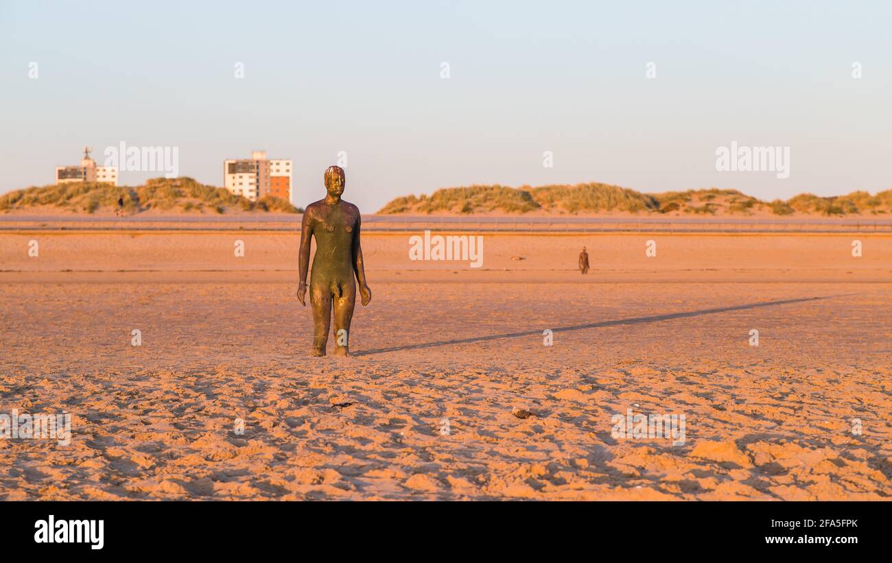 Lunga ombra dietro un uomo di ferro al tramonto sulla spiaggia di Crosby nell'aprile 2021. Questo, e quello in background sono parte di un altro luogo, l'installazione ART Foto Stock