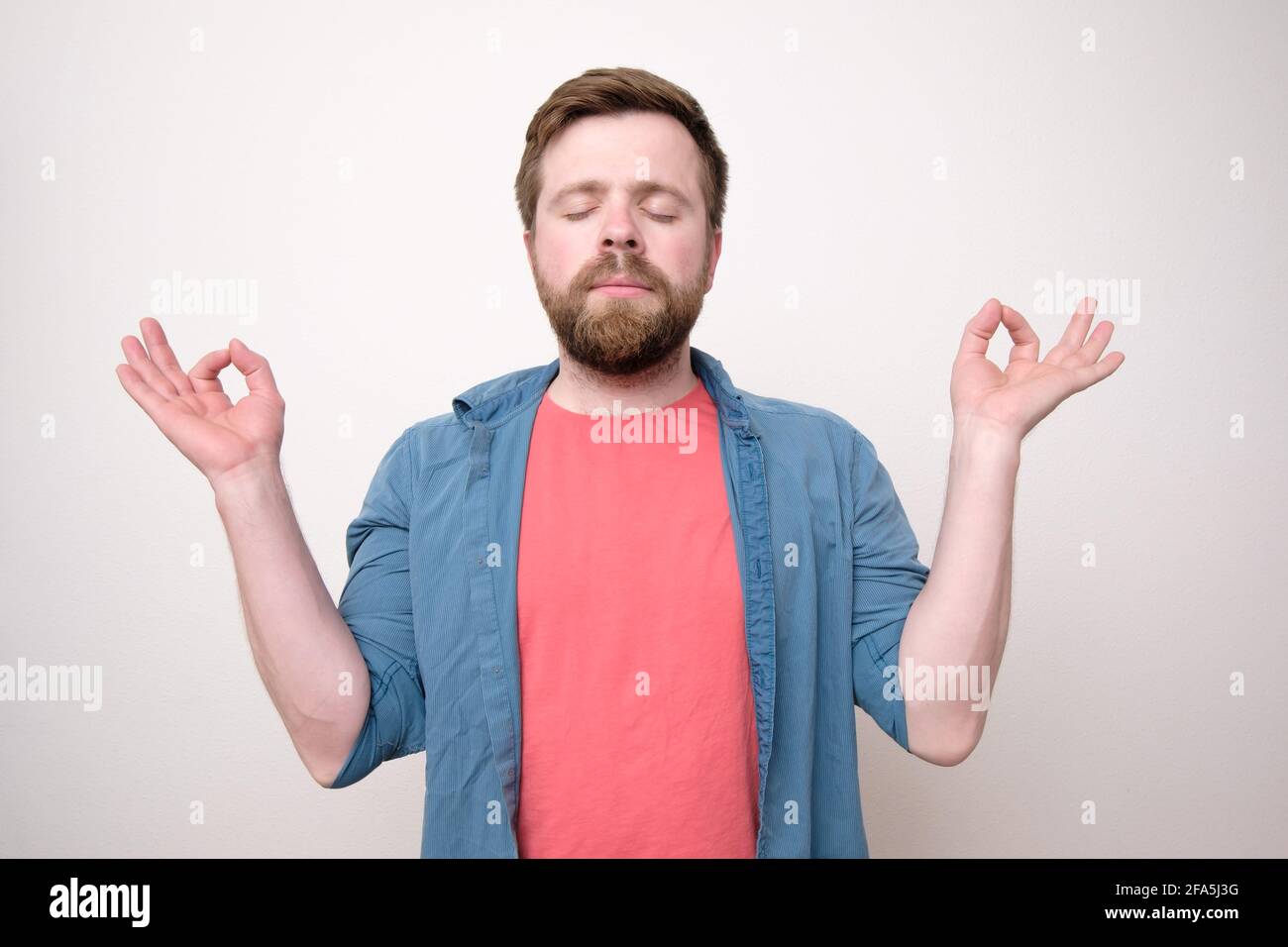 Attraente, calmo, rilassato uomo bearded con occhi chiusi, che medita e cerca di trovare armonia ed equilibrio. Sfondo bianco. Foto Stock