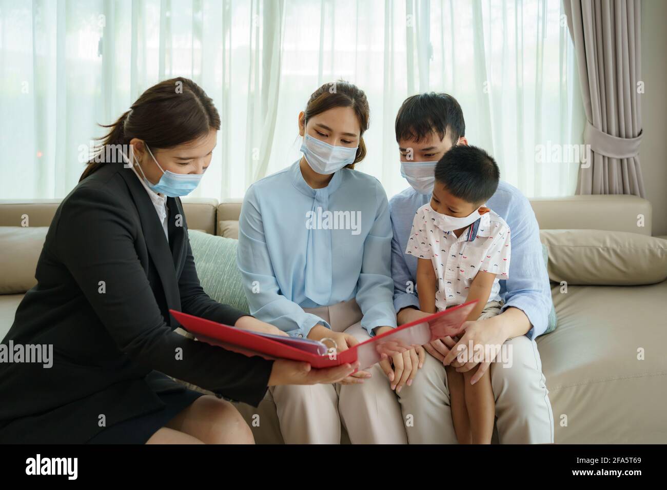 L'intermediario assicurativo della donna asiatica sta offrendo i particolari della copertura di assicurazione contro le malattie per COVID-19 alla famiglia asiatica con il padre, la madre ed il figlio nei loro livi Foto Stock