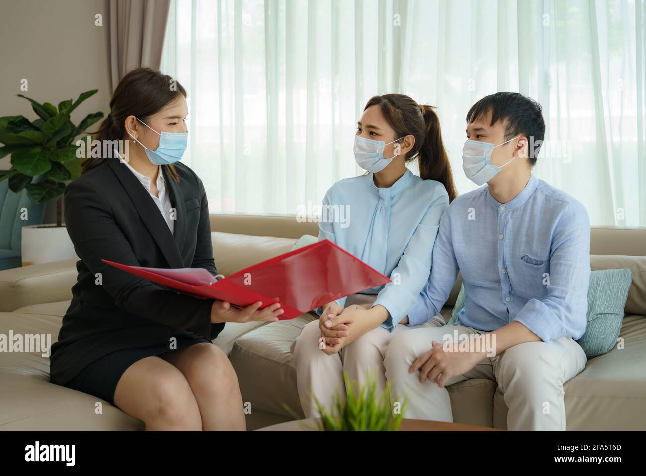L'intermediario assicurativo della donna asiatica sta offrendo i particolari della copertura di assicurazione contro le malattie per COVID-19 alla coppia asiatica nei loro soggiorni a casa. Foto Stock