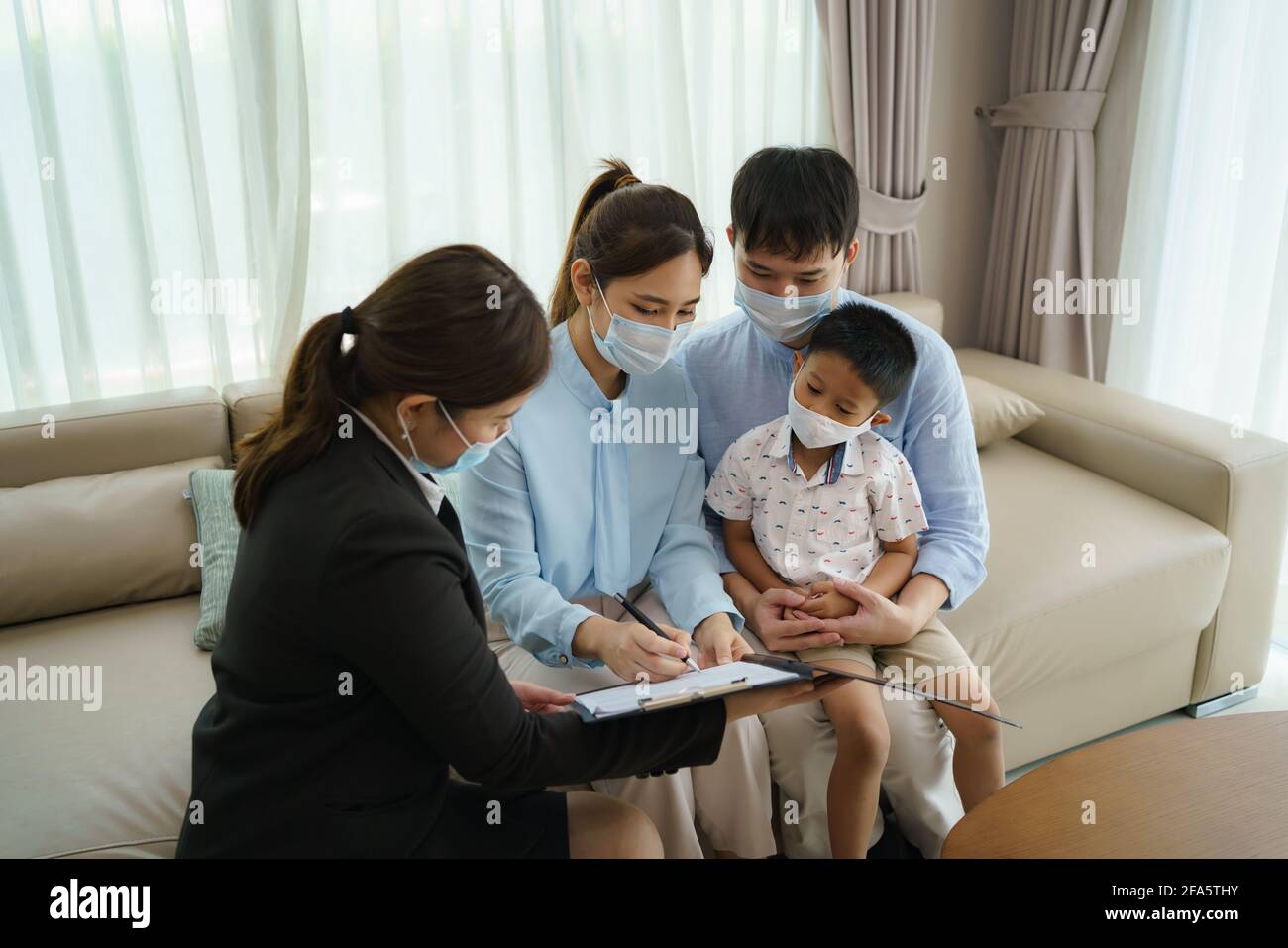 L'intermediario assicurativo della donna asiatica sta offrendo i particolari della copertura di assicurazione contro le malattie per COVID-19 alla famiglia asiatica con il padre, la madre ed il figlio nei loro livi Foto Stock