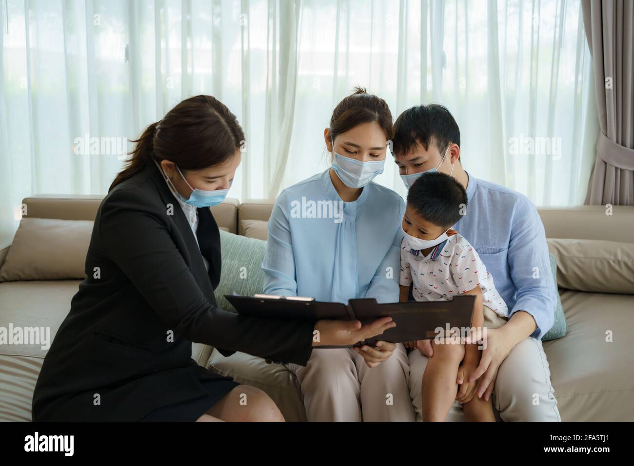 L'intermediario assicurativo della donna asiatica sta offrendo i particolari della copertura di assicurazione contro le malattie per COVID-19 alla famiglia asiatica con il padre, la madre ed il figlio nei loro livi Foto Stock