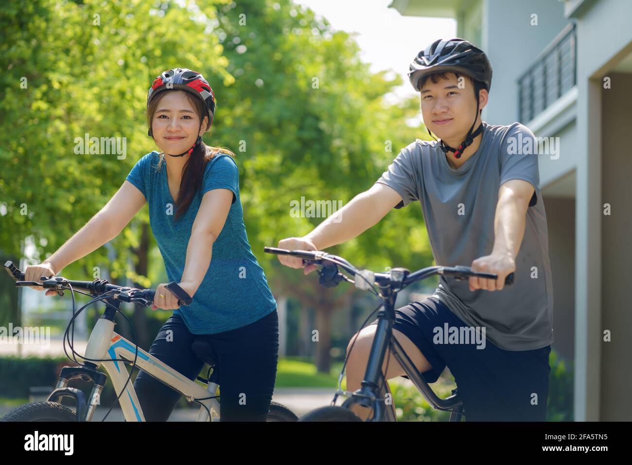 Coppia asiatica che indossa un casco mentre si prepara per un giro in bicicletta intorno al suo quartiere per la salute quotidiana e il benessere, sia fisico che mentale. Foto Stock
