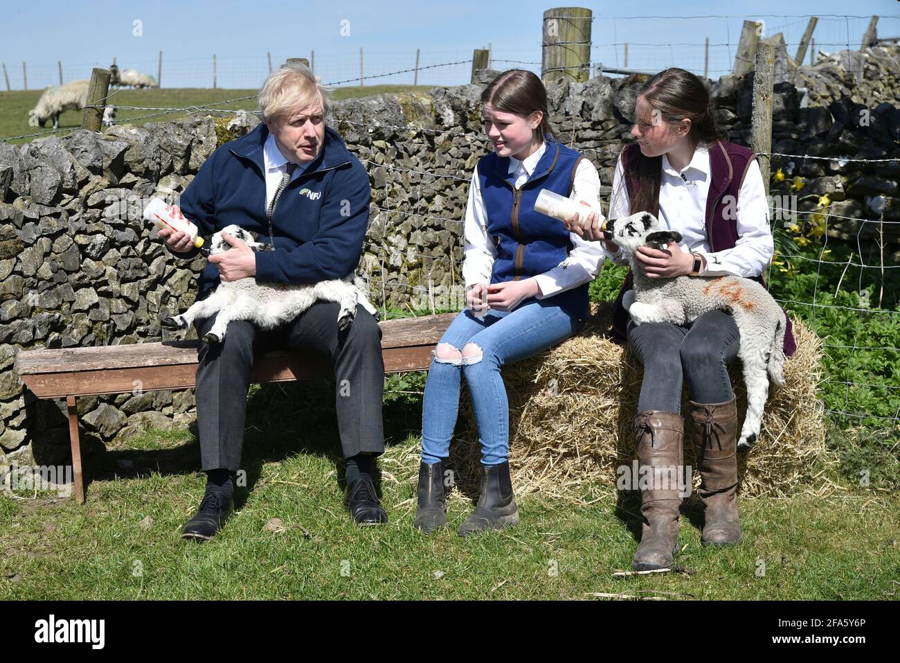 Il primo ministro Boris Johnson alimenta un agnello con Hayley Fairfax e Sarah Fairfax (a destra) durante una visita alla fattoria di Moor a Stoney Middleton, nel nord del Derbyshire sulla pista elettorale locale. Data immagine: Venerdì 23 aprile 2021. Foto Stock