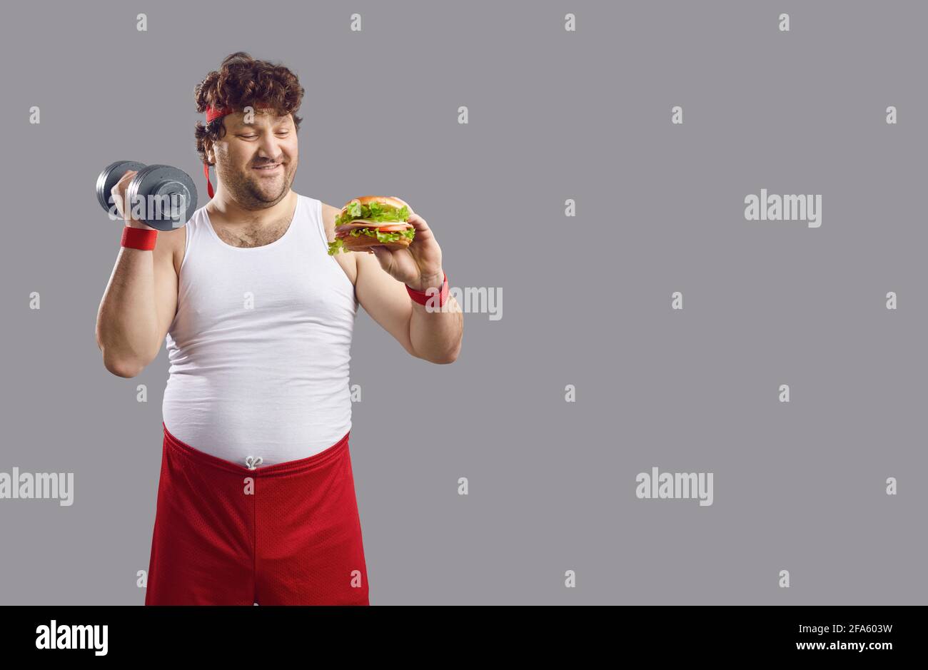 Divertente uomo in sovrappeso comico con manubri e hamburger studio isolato verticale Foto Stock