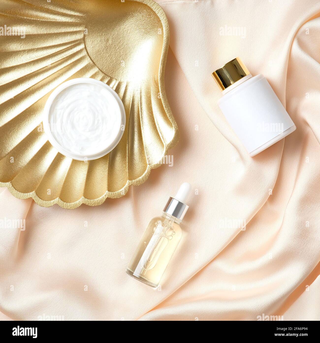 Set cosmetico di lusso e conchiglia dorata su sfondo in seta color pesca. Prodotti per la cura della pelle, design, branding. Foto Stock