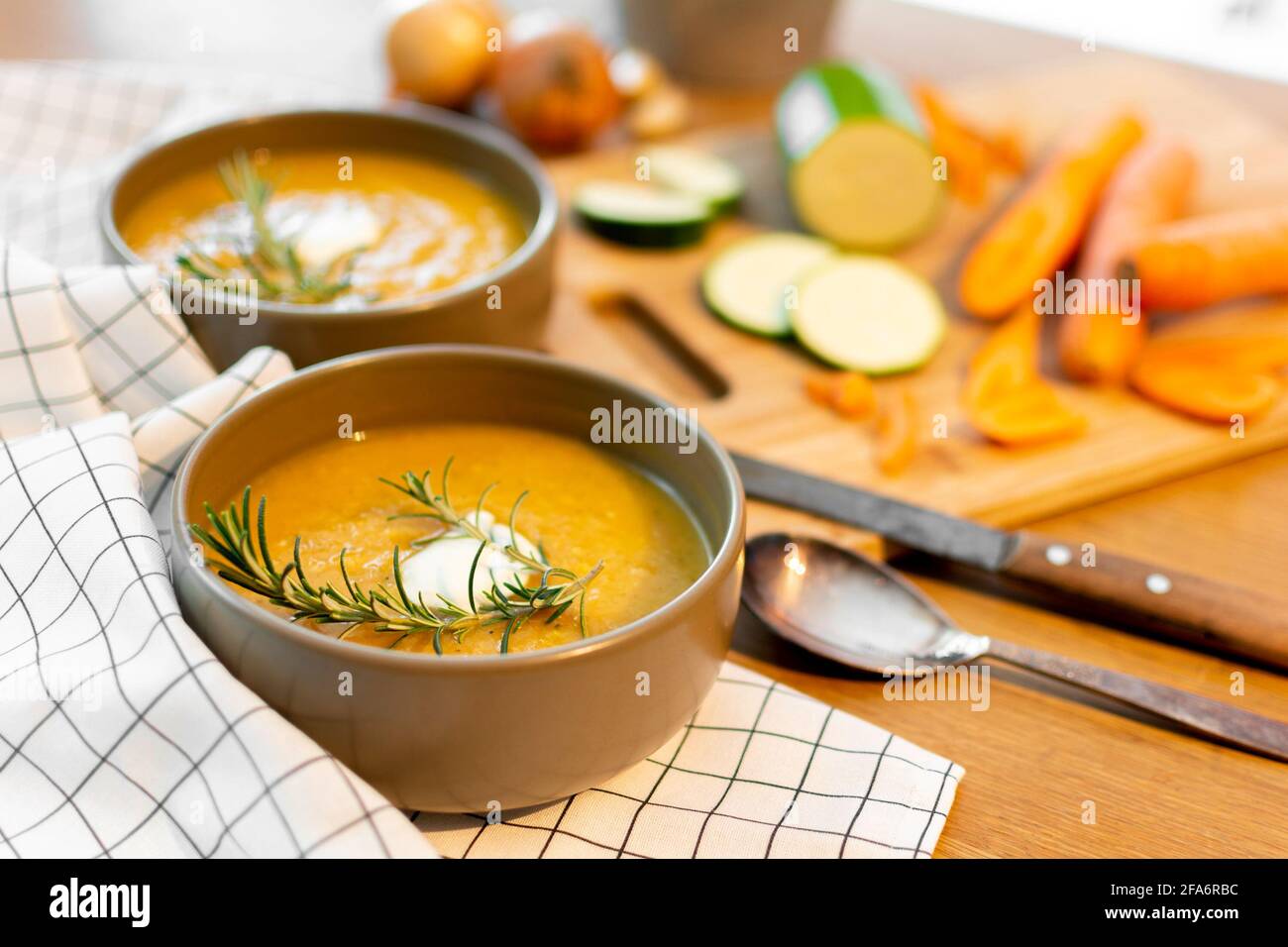Un bel pasto casalinga contenente una zuppa di verdure fresche con carote e zucchine e cipolle servite su un vecchio tavolo di legno con molta guarnitura. Foto Stock