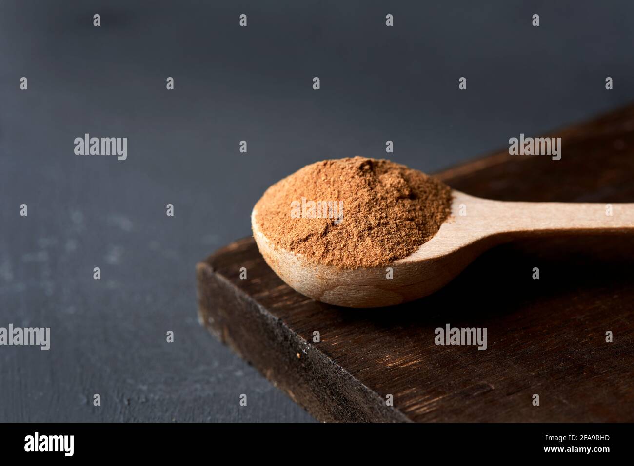 primo piano di un cucchiaio di legno pieno di polvere di camu-camu su un vassoio di legno scuro, posto su una superficie di colore grigio scuro Foto Stock