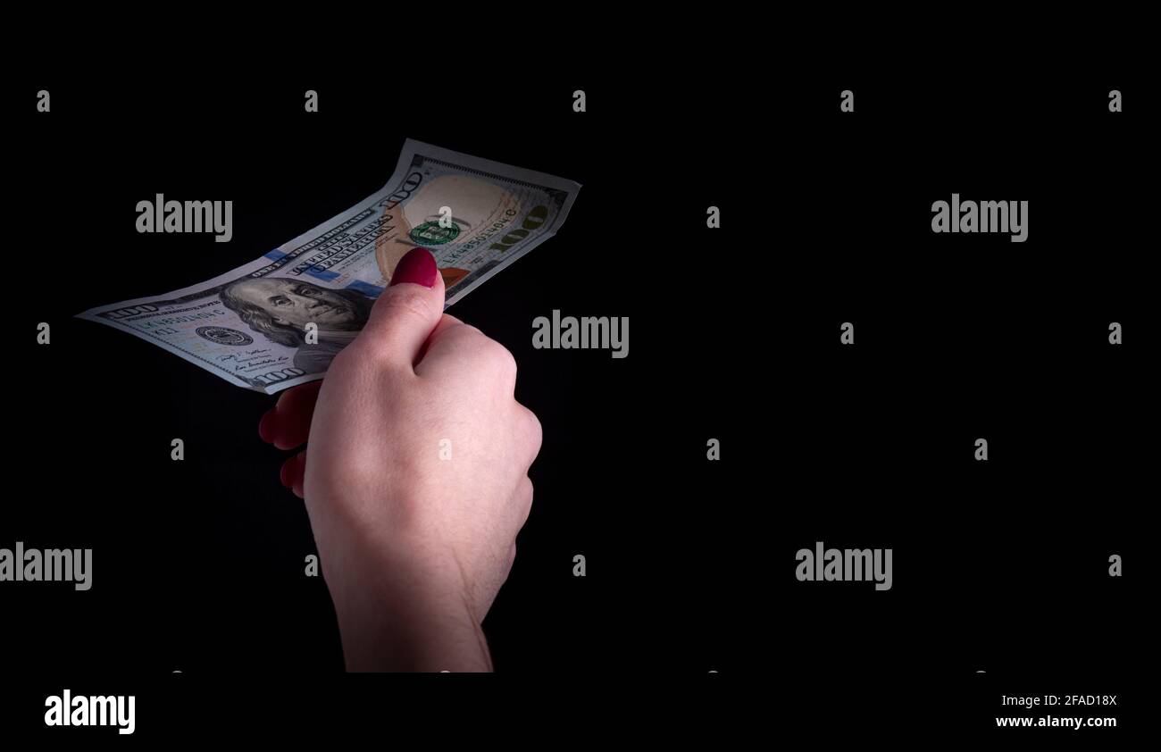 una mano della donna tiene fuori una fattura del dollaro su un sfondo nero Foto Stock