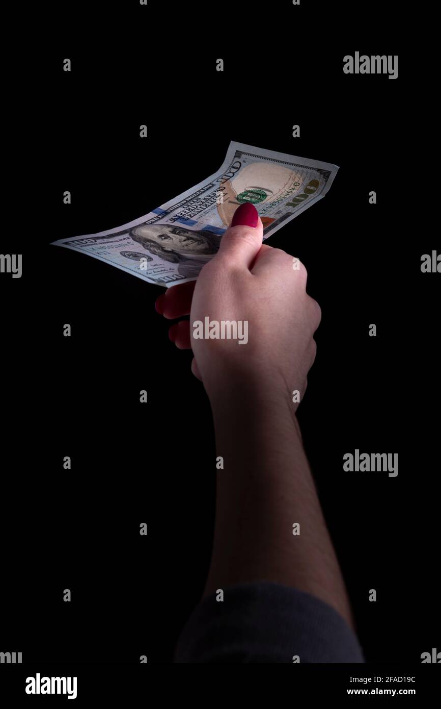 una mano della donna tiene fuori una fattura del dollaro su un sfondo nero Foto Stock