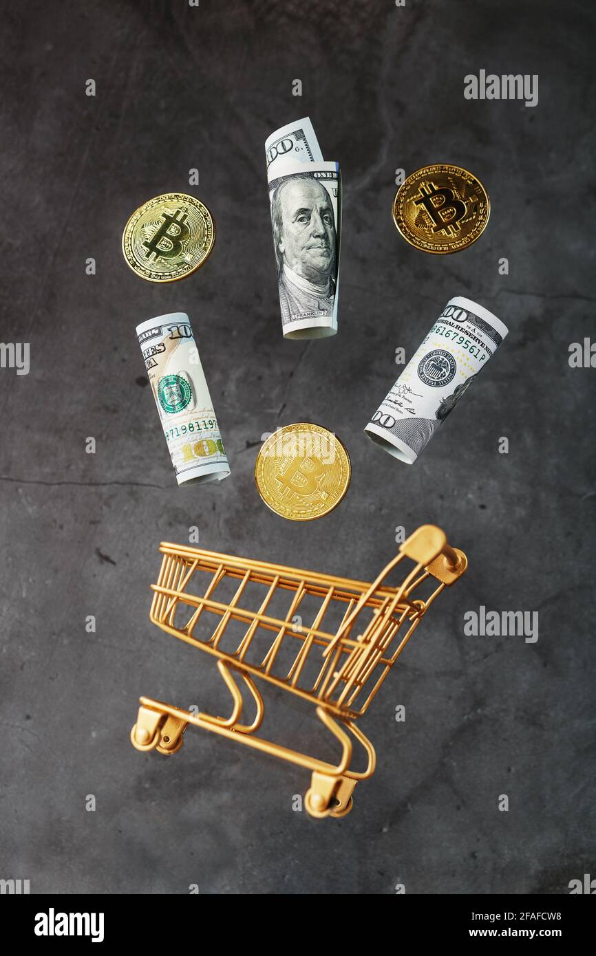 Mini cart oro con monete di bitcoin e dollari USA in un volo di levitazione su uno sfondo scuro. Un concetto di shopping per le imprese di criptovaluta, fin Foto Stock