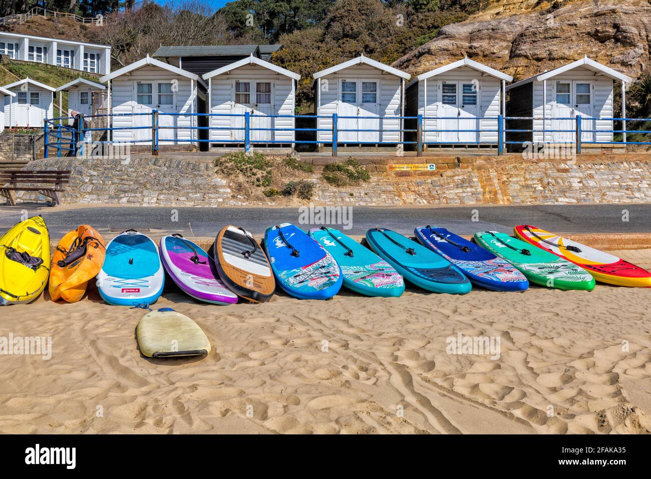 Tavole da surf colorate, tavole da surf, con capanne sulla spiaggia a Branksome Dene Chine, Poole, Dorset UK in una calda giornata di sole nel mese di aprile Foto Stock
