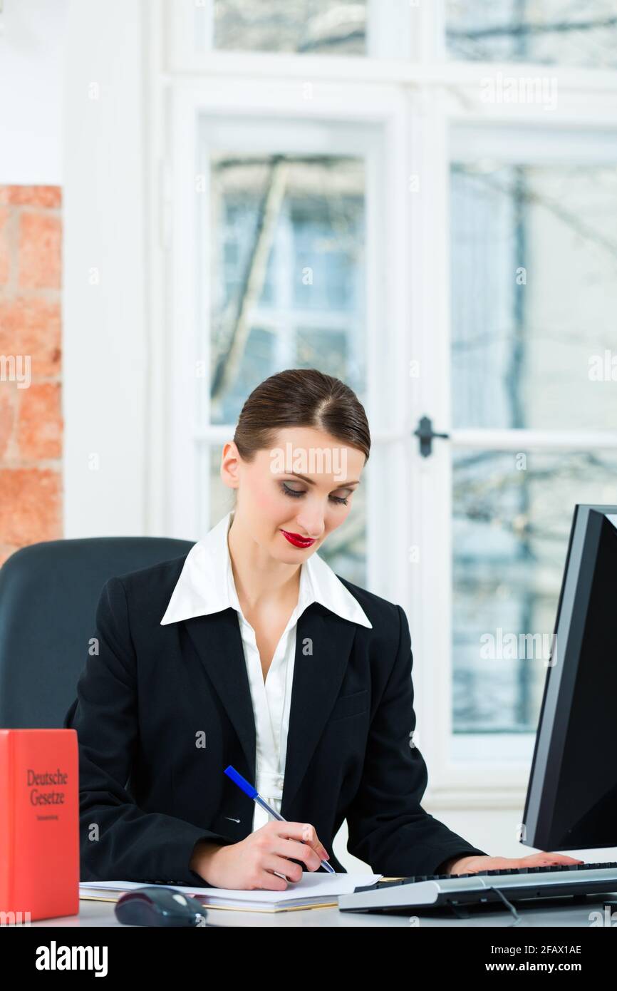 Giovane avvocato lavorando nel suo ufficio, lei è seduta dietro le cartelle la scrittura in un file Foto Stock