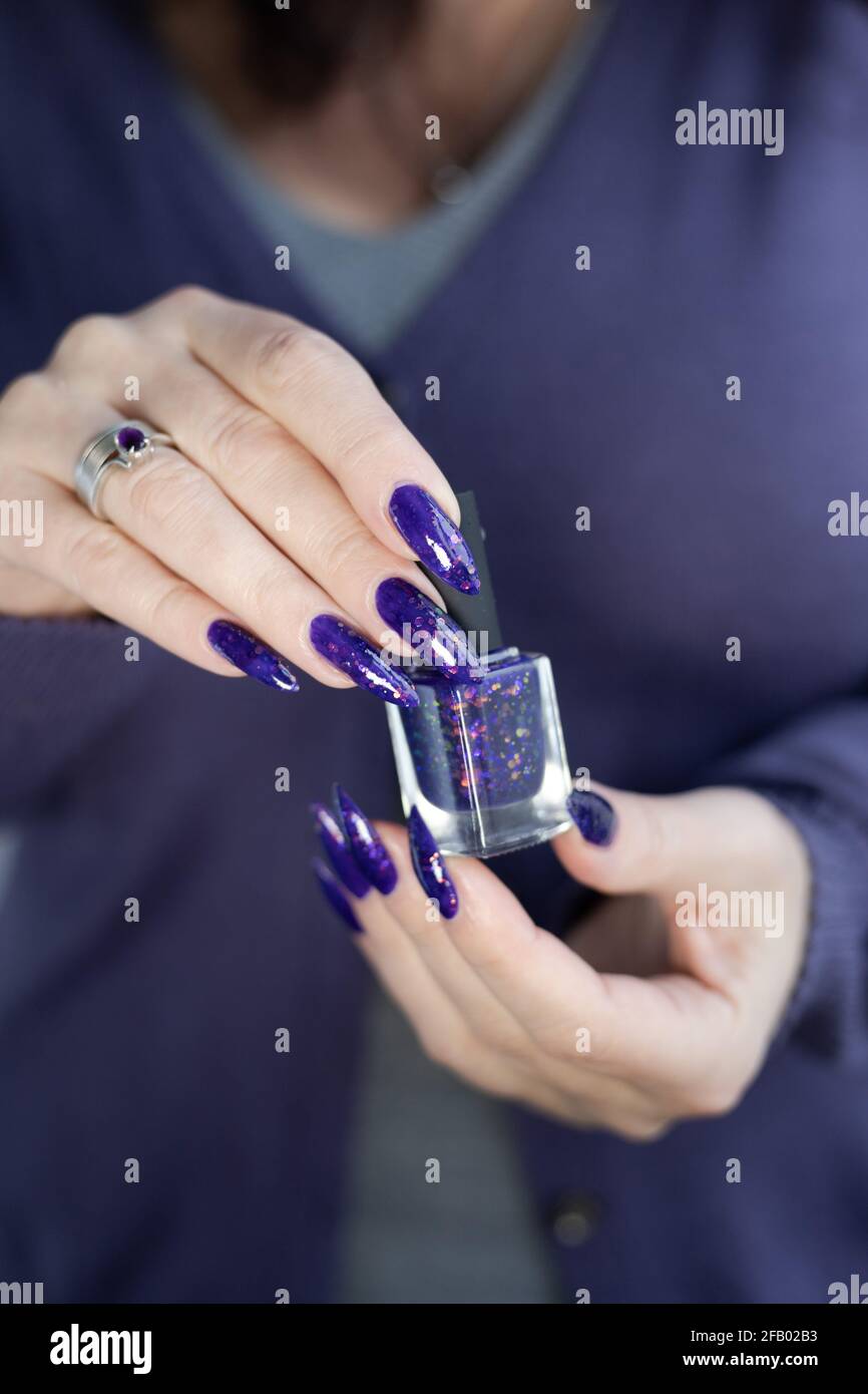 Mano femminile con unghie lunghe e manicure lilla viola tiene una bottiglia  di smalto per unghie Foto stock - Alamy