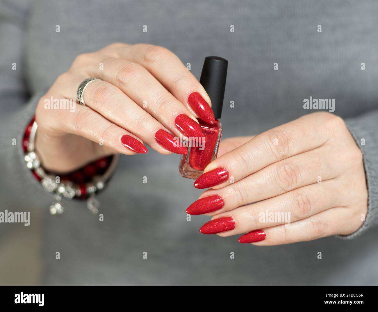 Mani della donna con unghie lunghe e una bottiglia di brillante smalto rosso  per unghie Foto stock - Alamy