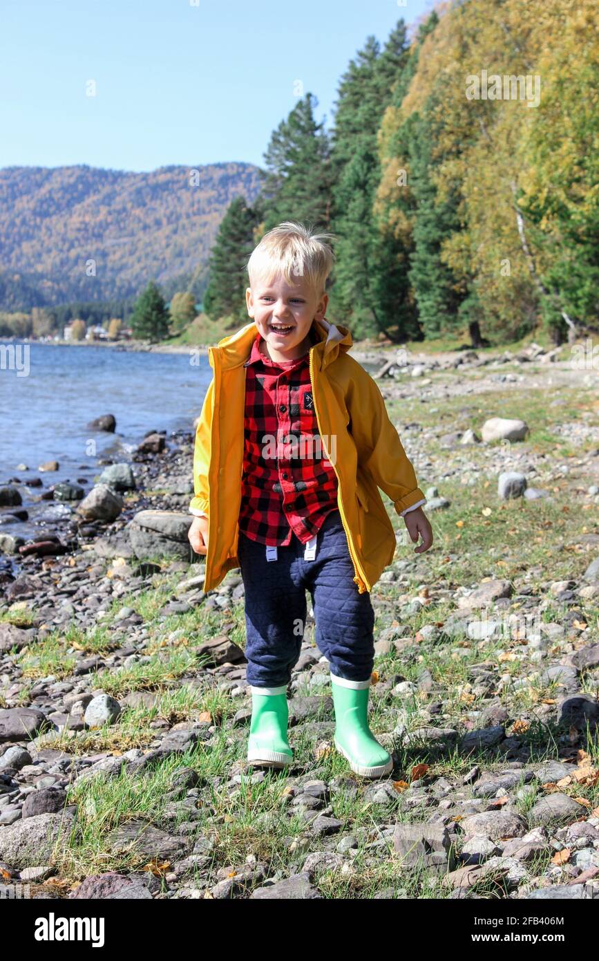 un bambino dai capelli leggeri, in piedi sulla riva di un lago di montagna. Foto Stock