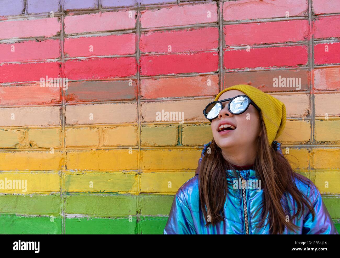 La ragazza adolescente si trova vicino a una parete arcobaleno-colorata all'esterno. Concetto di auto-amore. Stile di vita del bambino. Foto Stock