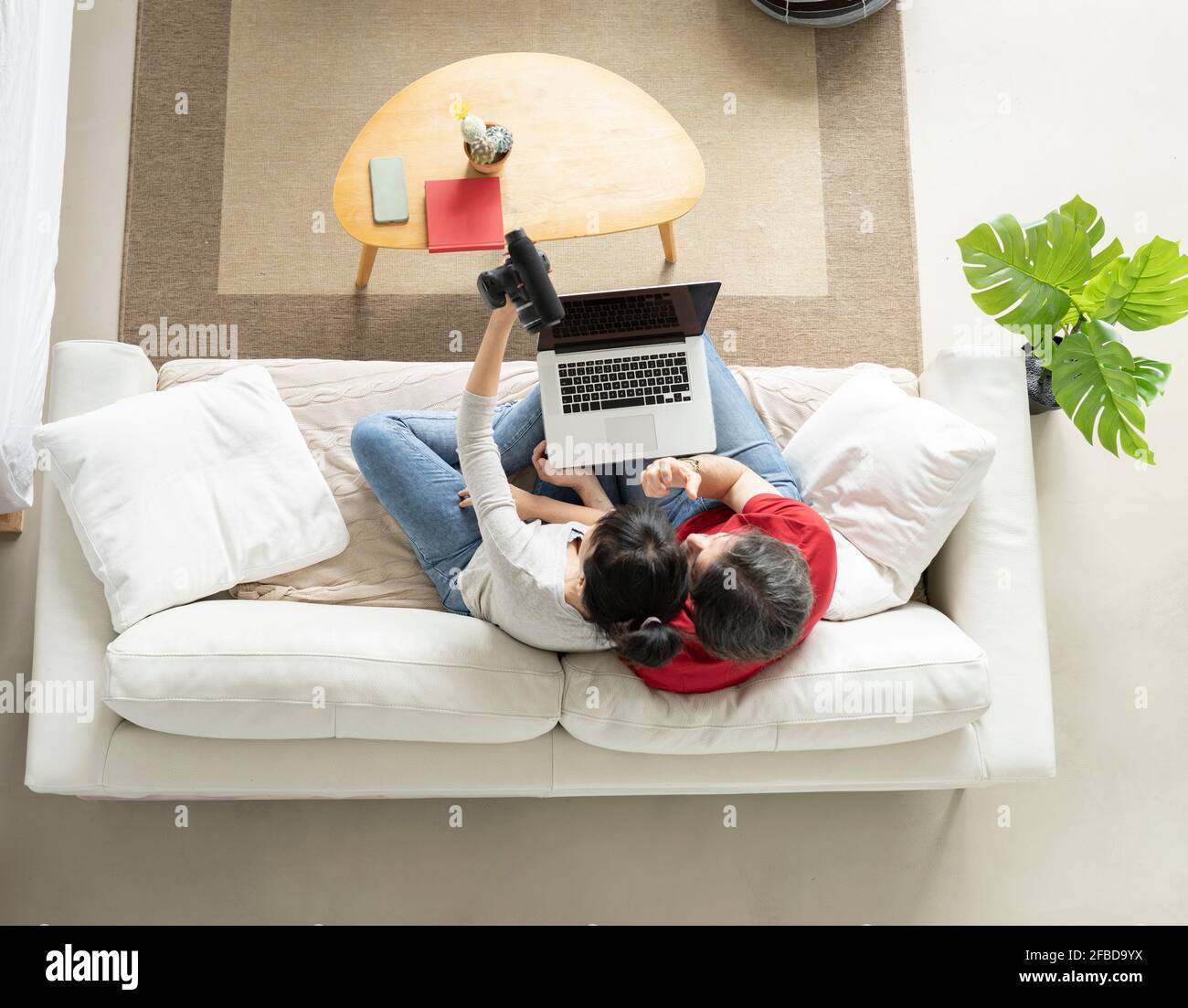 Uomo con notebook seduto da una donna che tiene la fotocamera digitale mentre vlogging a casa Foto Stock