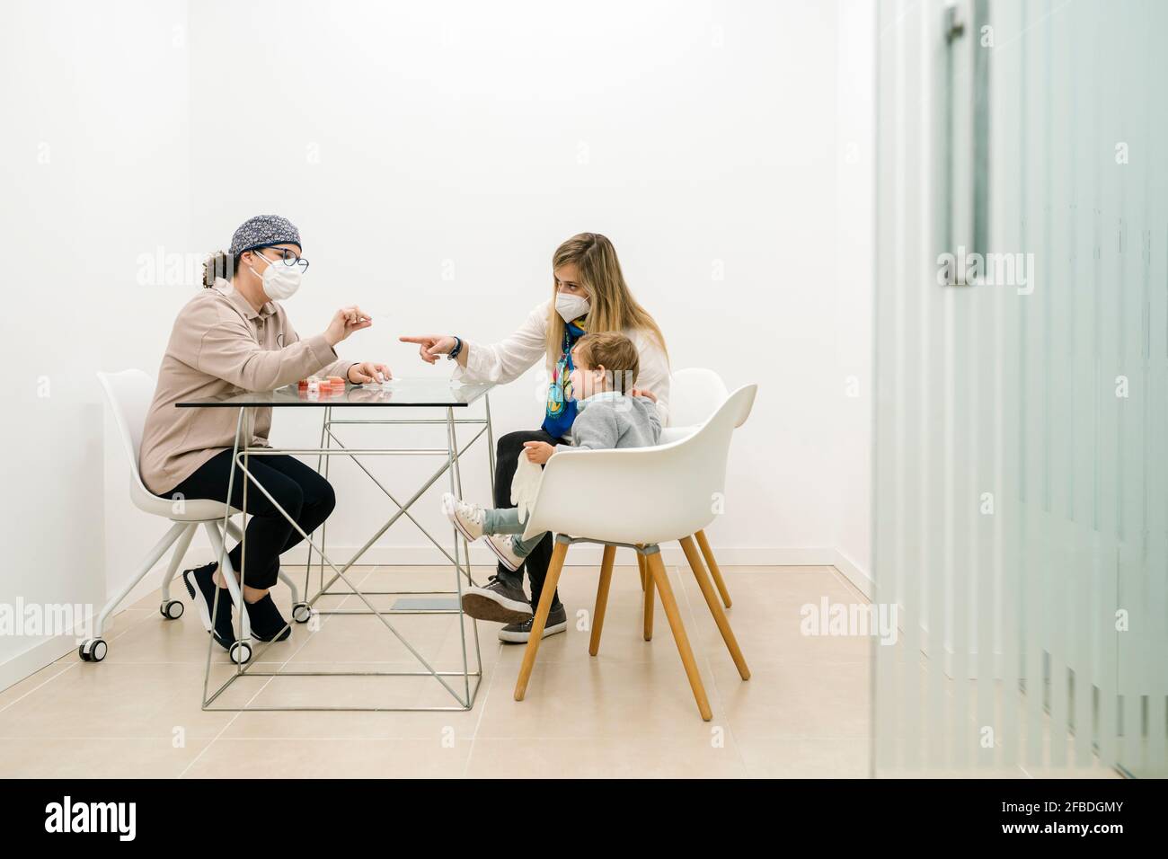Dentista pediatrico che parla con il ragazzo seduto con la madre in ufficio Foto Stock