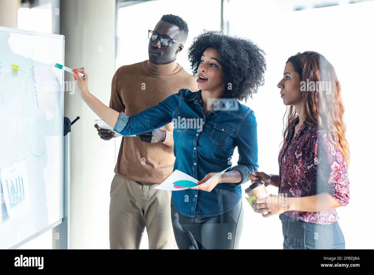 Donna d'affari che spiega la strategia di affari ai colleghi sopra il bordo bianco a. ufficio Foto Stock