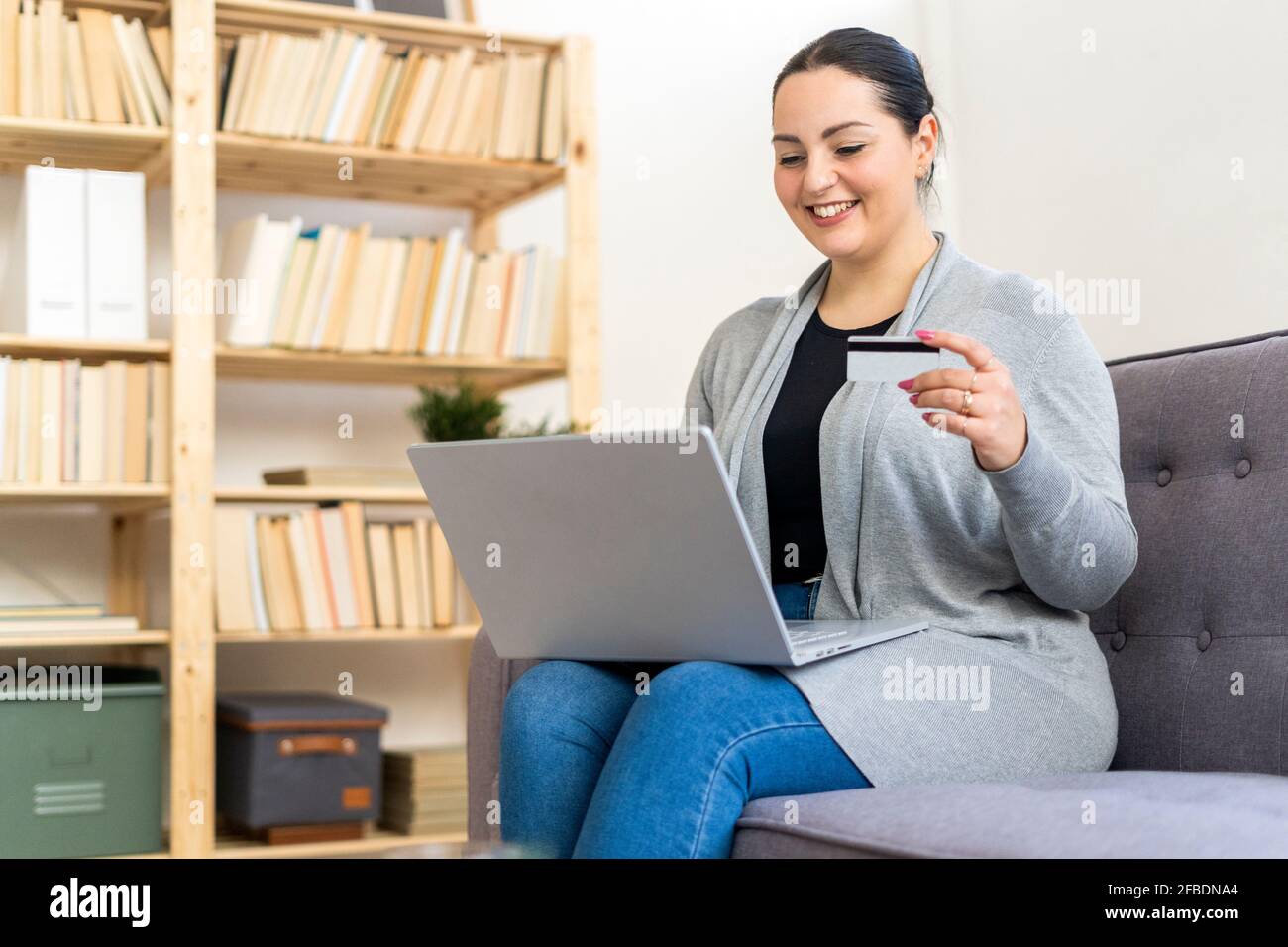 Donna sorridente che tiene la carta di credito mentre lo shopping in linea con il laptop a casa Foto Stock