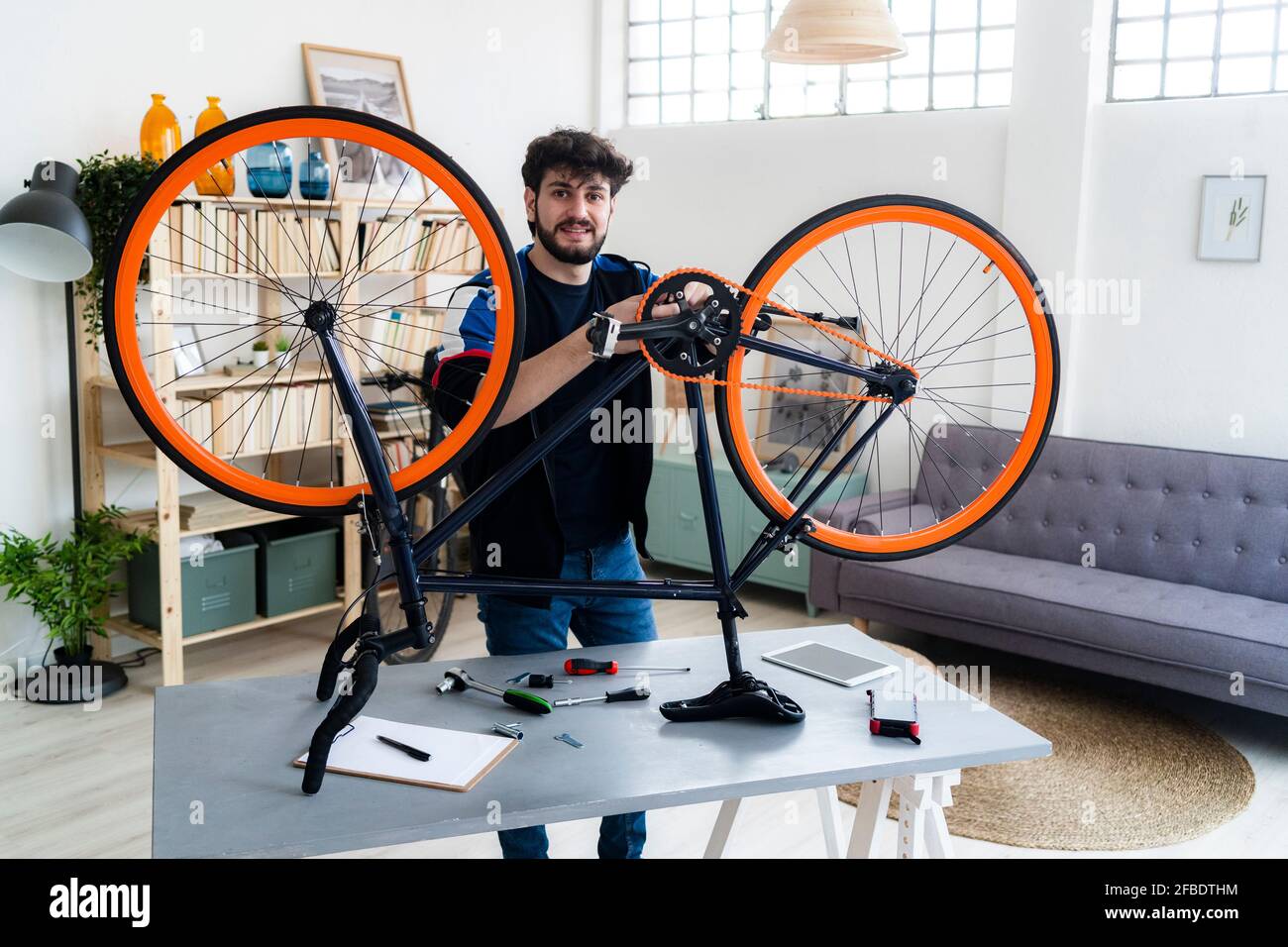 Uomo sorridente che ripara la bicicletta a casa Foto Stock