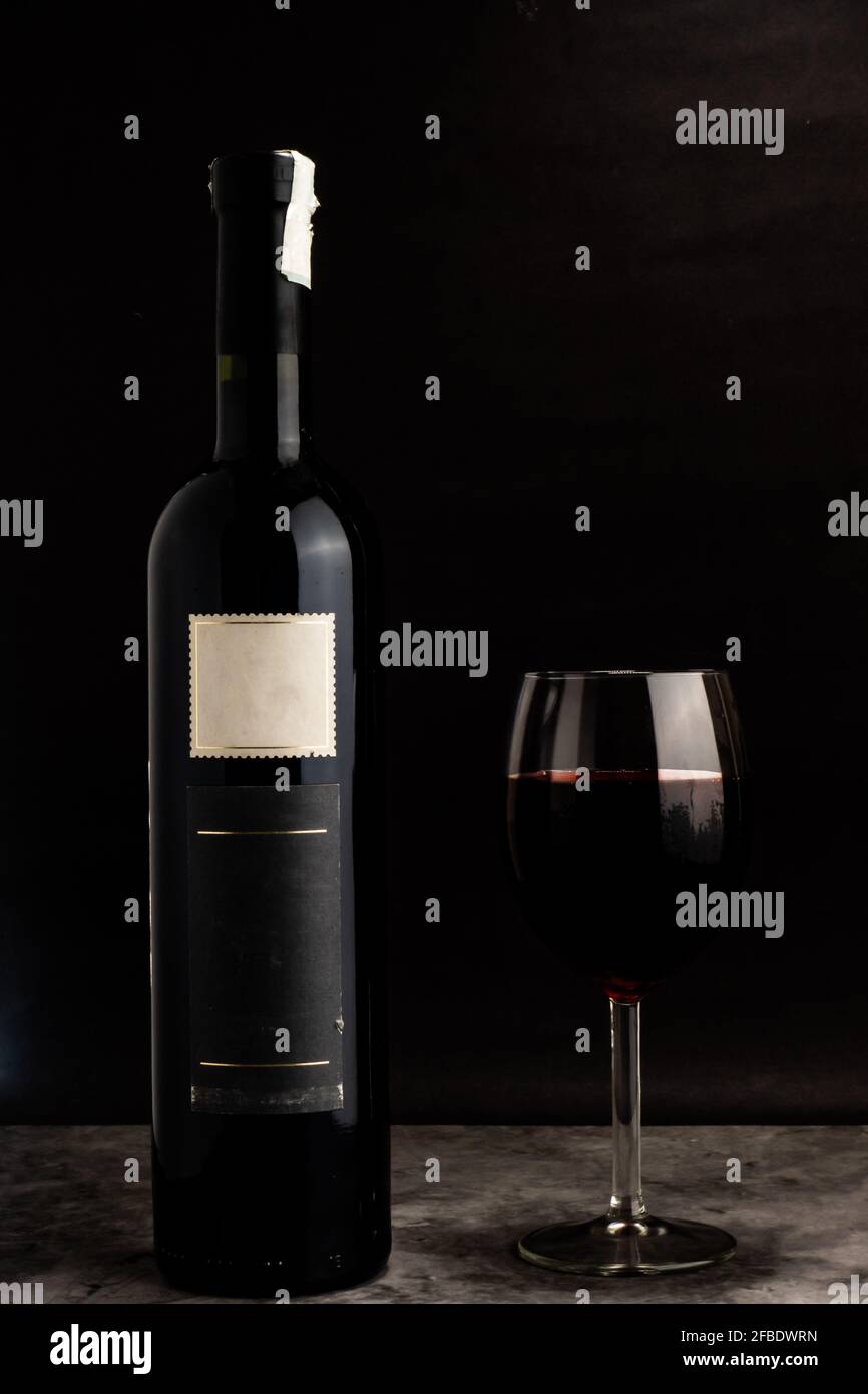 una bottiglia di vino senza nome e un bicchiere di vino con un bel fondo nero, come nel concetto di vino commerciale Foto Stock