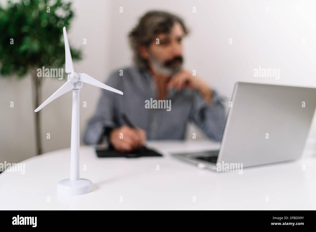 Turbina eolica su tavolo mentre l'uomo d'affari lavora in background a. ufficio domestico Foto Stock