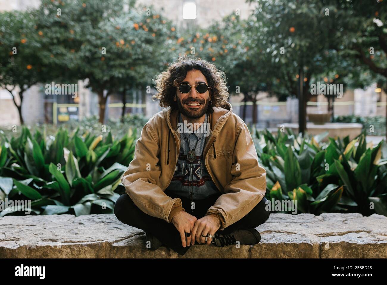 Uomo sorridente con gambe incrociate sedute su un muro di contenimento Foto Stock