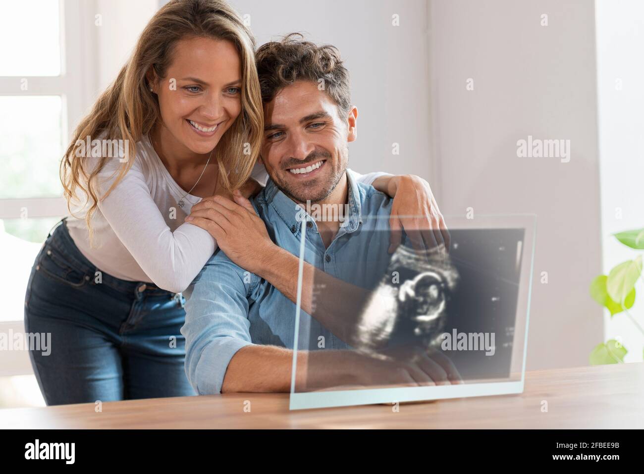 Una coppia affettuosa che guarda l'immagine ecografica su uno schermo trasparente all'indirizzo casa Foto Stock