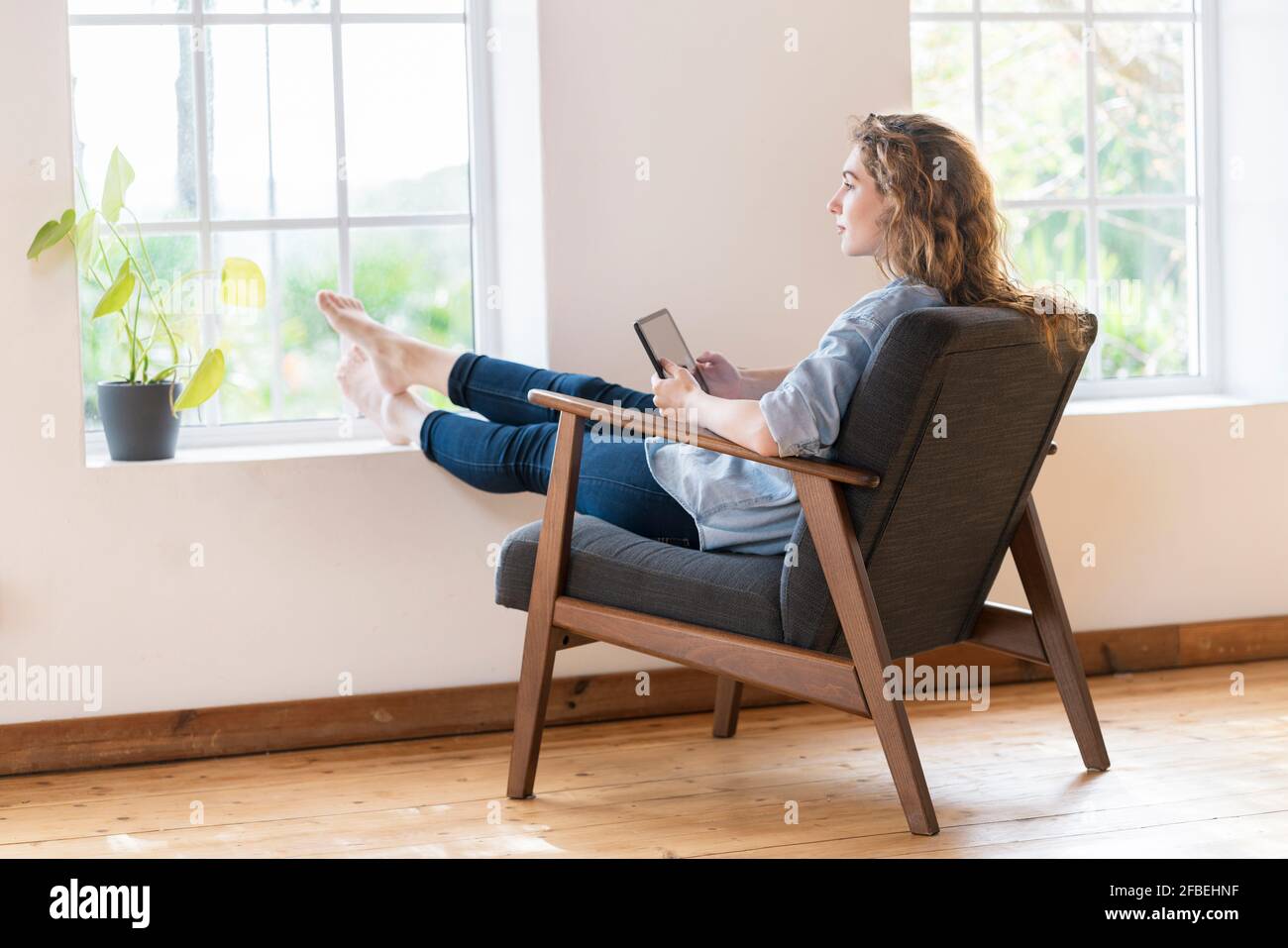Giovane donna che tiene un tablet digitale mentre si siede sulla poltrona casa Foto Stock