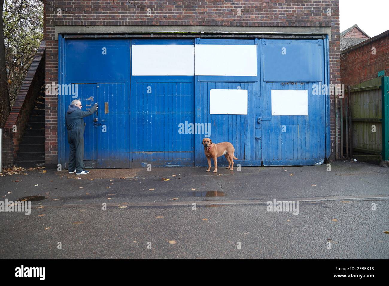 Meccanico maschio che apre la porta del garage mentre cane in piedi strada Foto Stock