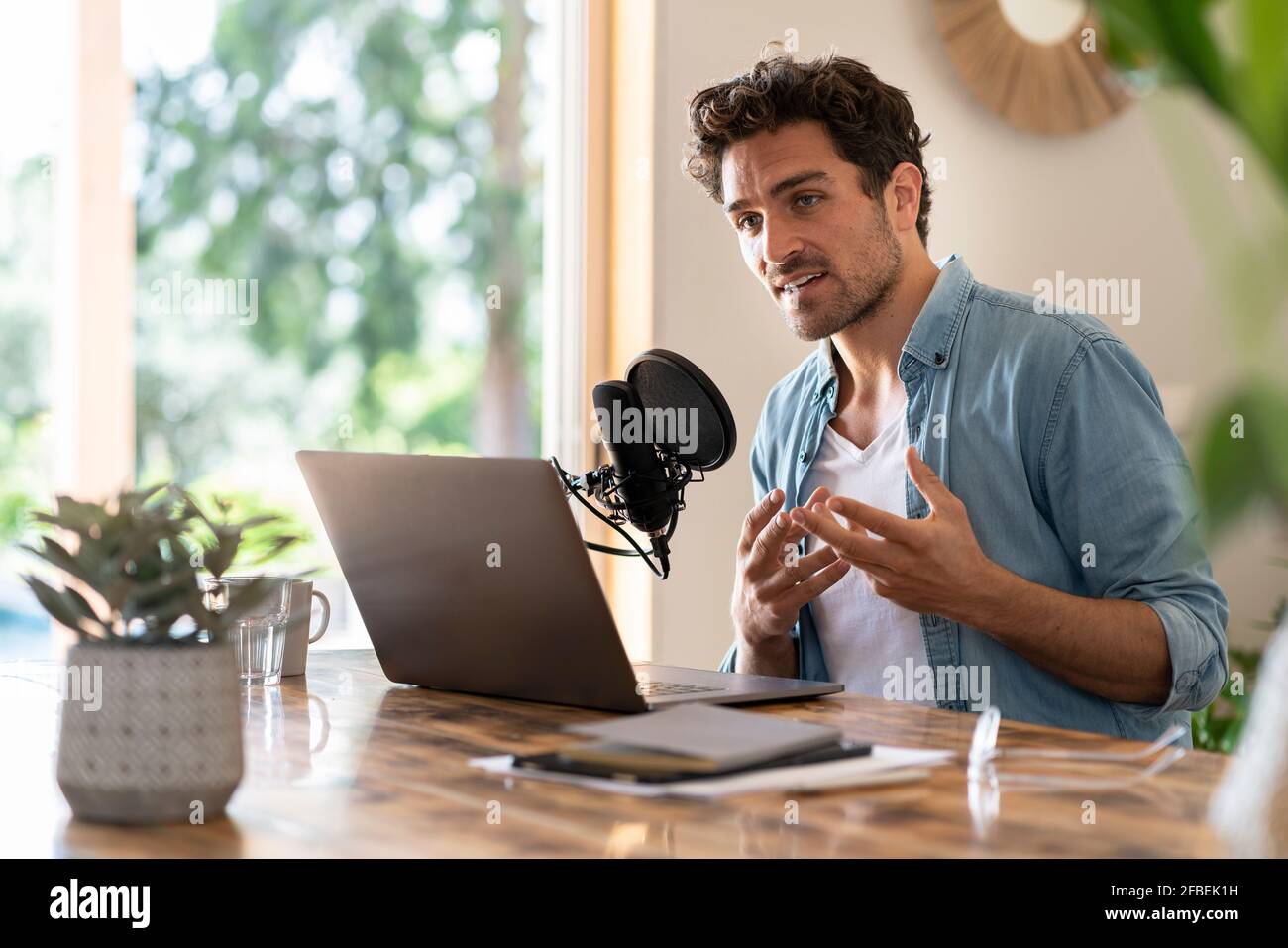 Lavoratore freelance maschile che guarda via mentre podcasting in ufficio domestico Foto Stock
