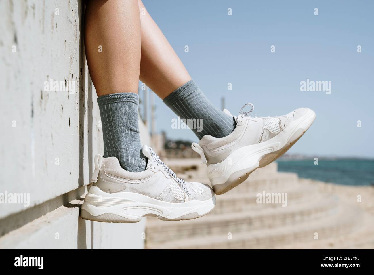 Donna mid adulta che penzolava i piedi mentre si siede su un muro di ritegno Foto Stock