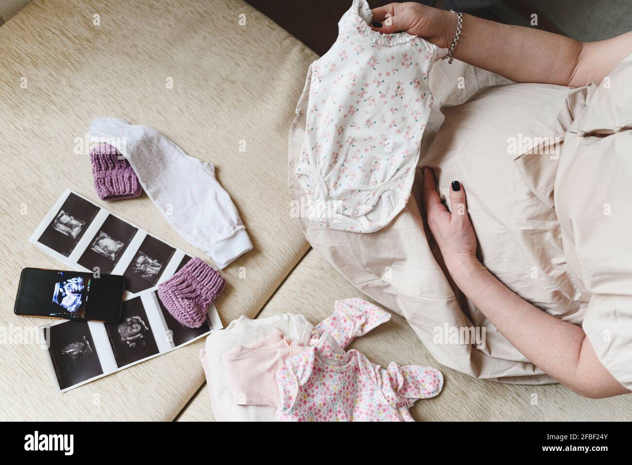 Donna incinta con scansione ecografica che tiene i panni del bambino mentre si siede a casa Foto Stock