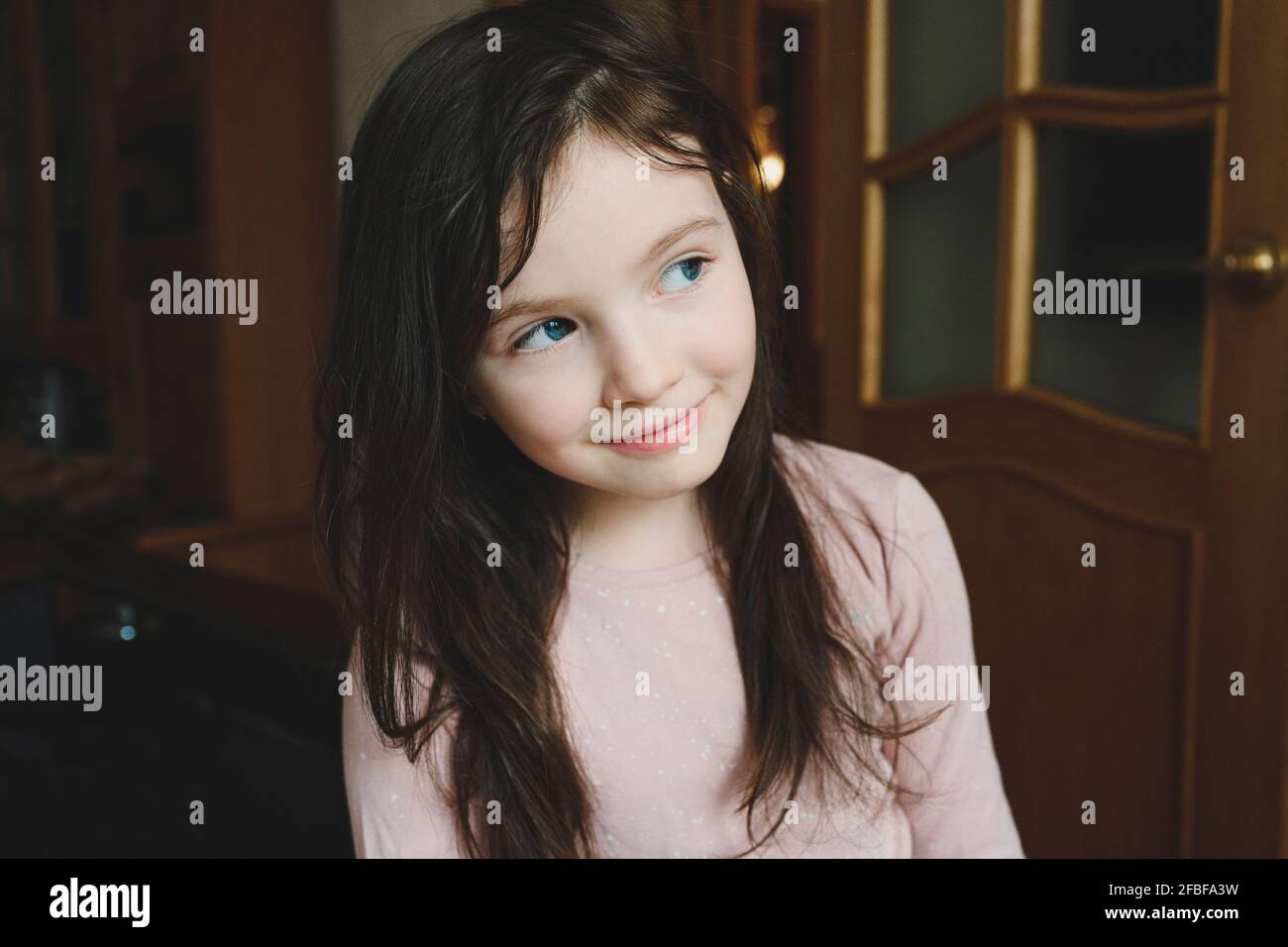 Ragazza curiosa con gli occhi blu che guardano via a casa Foto Stock