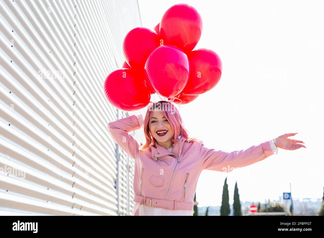 Donna felice con palloncini in piedi da parete di ferro corrugato su giorno di sole Foto Stock