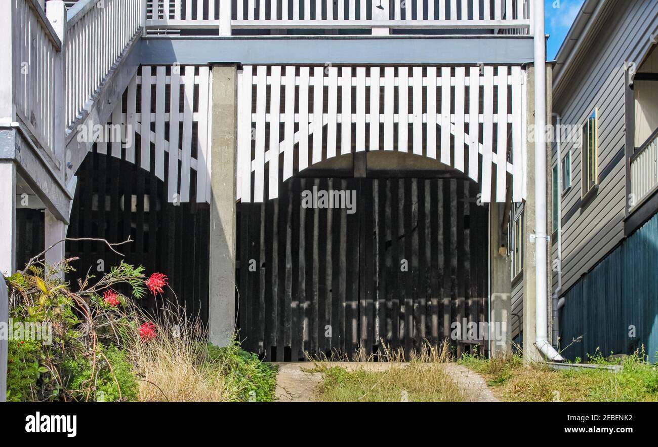 Closeup di carport-garage sotto una casa Queenslander con tavole bianche in un arco e vialetto diviso Foto Stock