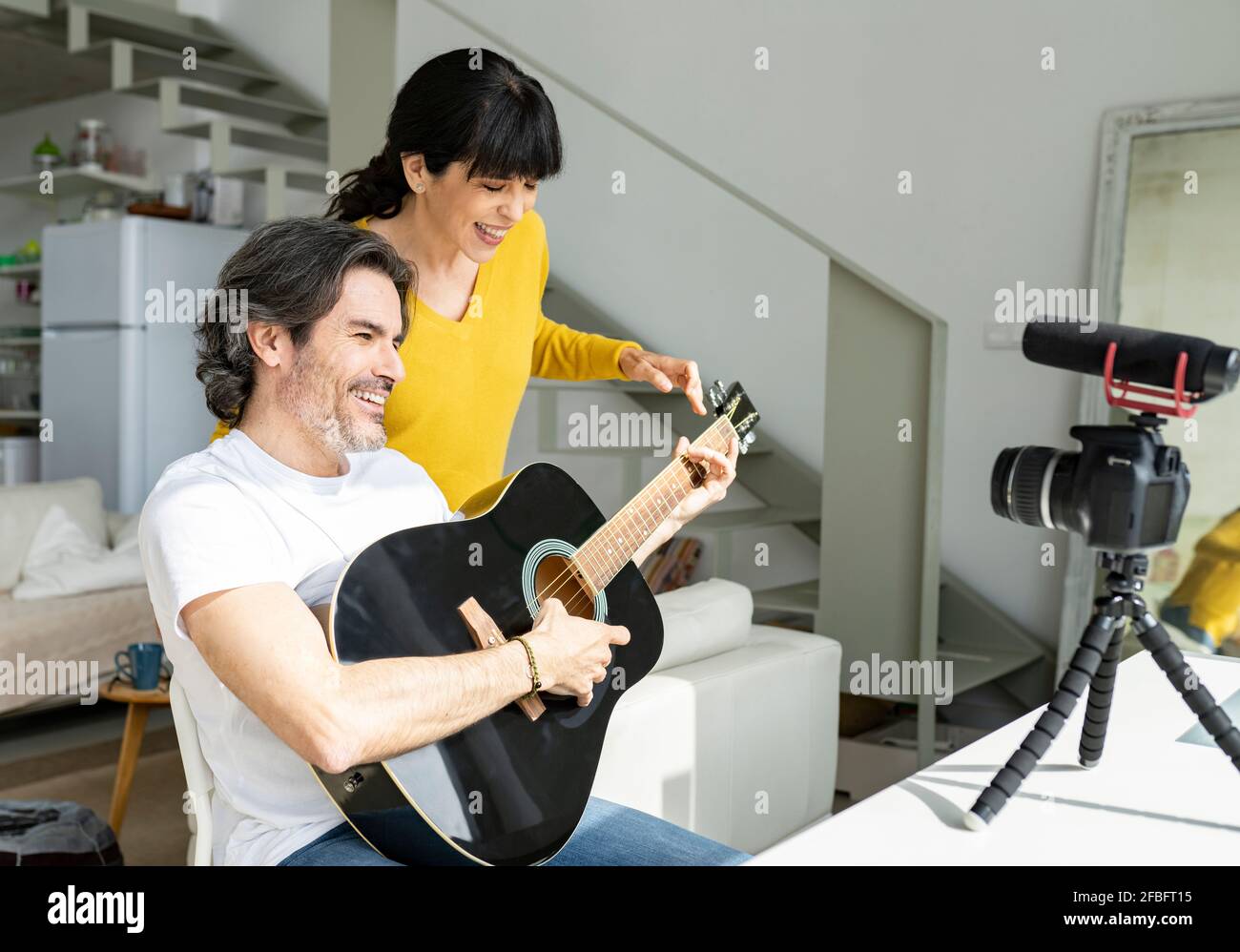 Coppia matura che suona la chitarra mentre vlogging attraverso la macchina fotografica digitale a. casa Foto Stock